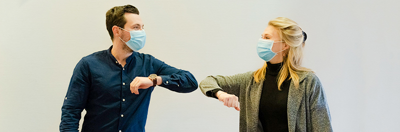 Two people wearing masks touching elbows