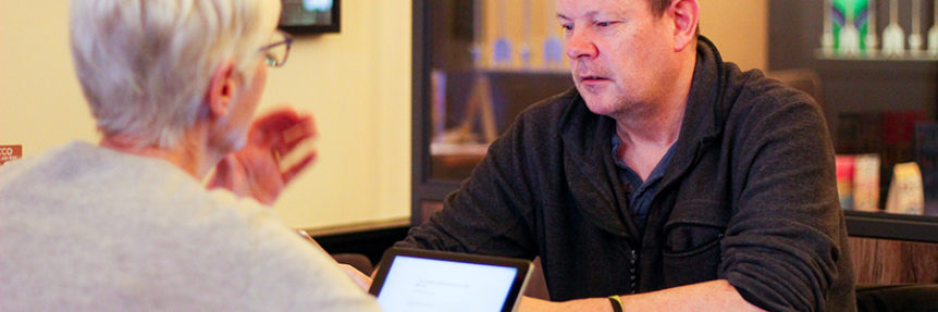 Two people sitting across from one another, using digital devices at a Reconnect digital group