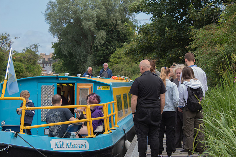 A group of people queuing on the pontoon to get onto the All Aboard canal boat