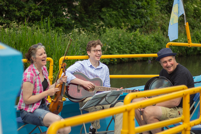 Three musicians playing instruments on the All Aboard canal boat