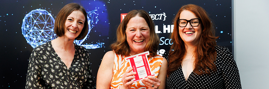 Three people smiling to camera at the Digital Health & Care Awards. The person in the middle is holding up an award.