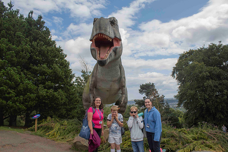 A group of young people on a Positive Transitions summer trip at Edinburgh Zoo, posing in front of a dinosaur statue