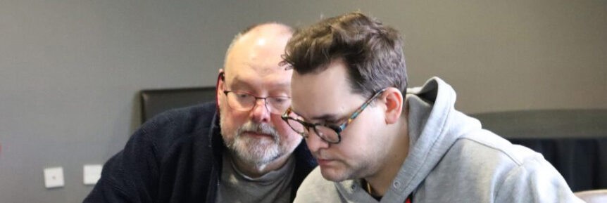 Two people sitting side by side looking down at a table