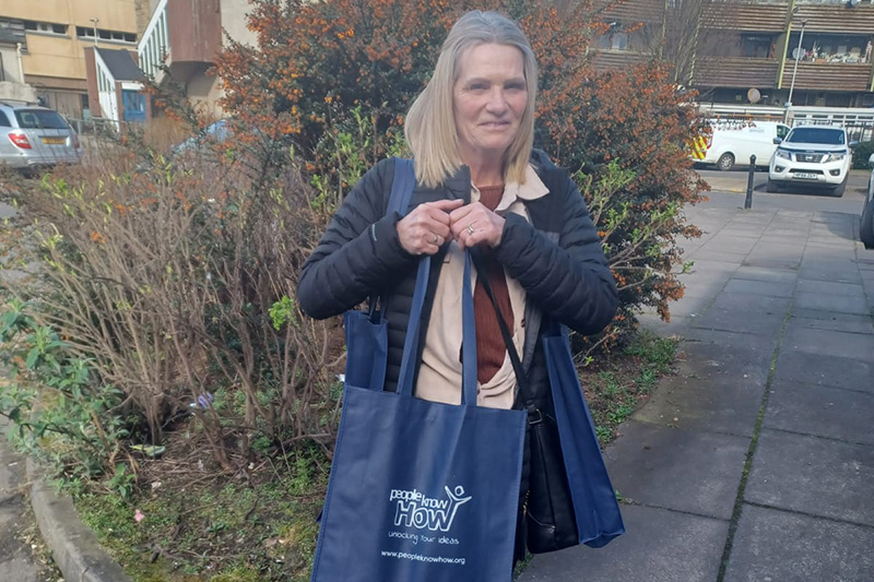 Yvonne standing outside holding a People Know How bag filled with laptops smiling to camera