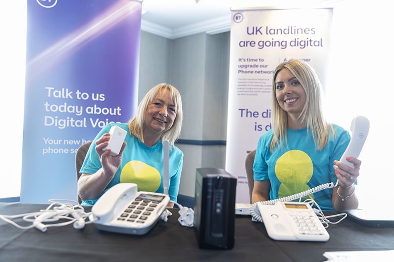 Two people sitting in front of telecomms equipment holding up landline telephones